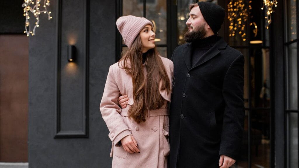 A couple dressed in stylish winter formal clothes, standing outdoors in cozy coats and hats, showcasing winter fashion.