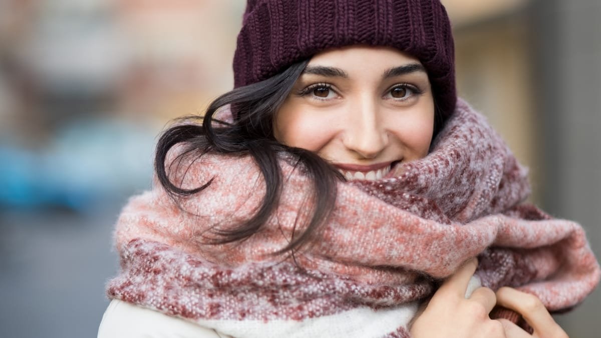 Woman smiling and wearing a cozy knit beanie and a warm scarf in a winter setting.