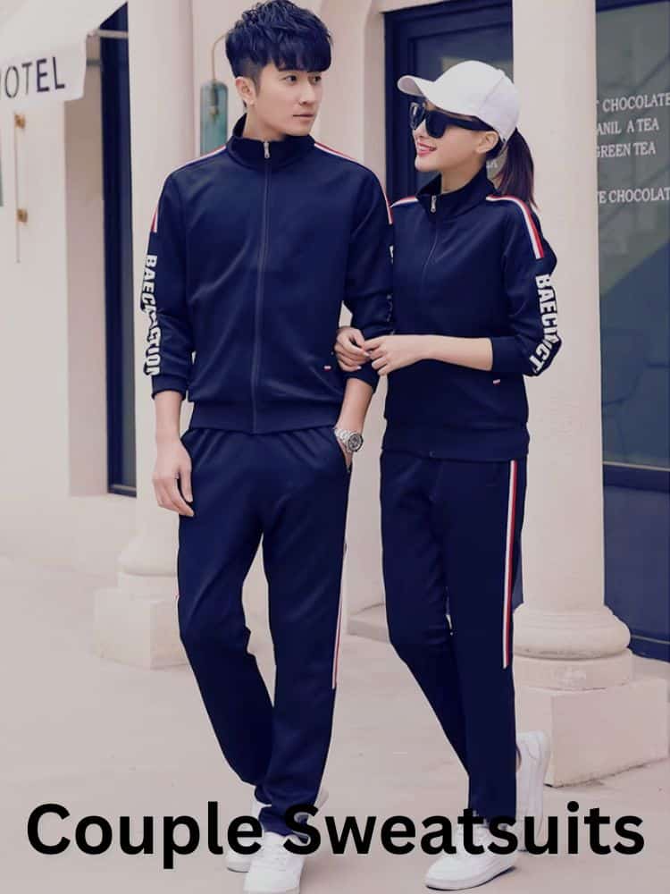 A couple wearing matching navy blue sweatsuits with red and white stripes on the sleeves and pants, smiling and walking together in a casual, relaxed setting.