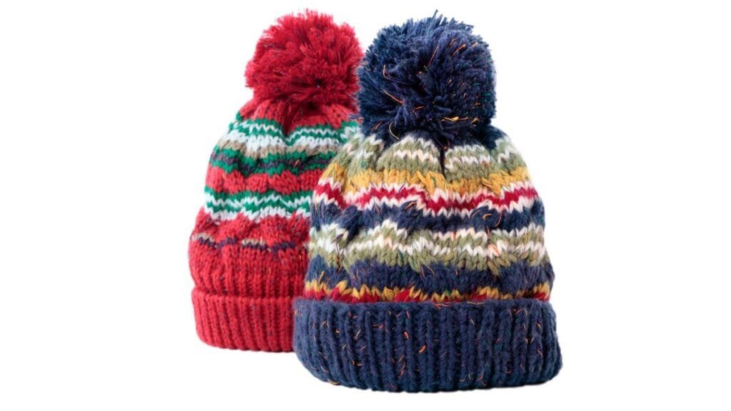 Two colorful knitted winter hats with pom-poms, one red with green, white, and blue stripes, and the other navy blue with multicolored zigzag patterns. Both hats feature ribbed cuffs and are designed to provide warmth and style for cold weather.