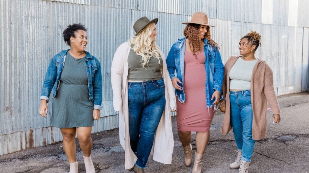 A group of four women, dressed in stylish casual outfits, walking together and smiling outdoors.