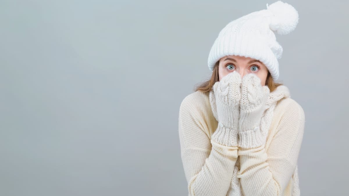 Woman wearing white winter clothes, hat, and gloves, covering her face with her hands in a cold-weather pose.