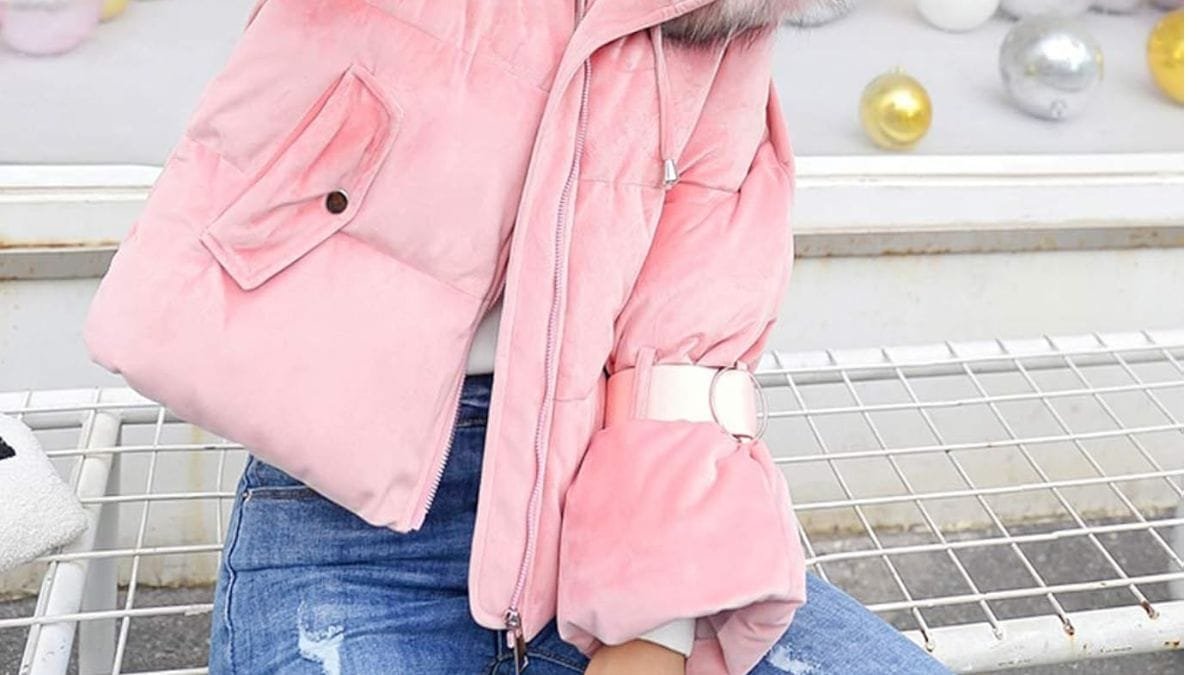 A woman wearing a pink puffer winter coat with a fur-lined hood and a white belt, paired with blue jeans.