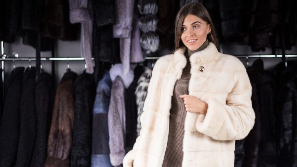 A woman models a luxurious white faux fur coat in a boutique filled with various fur coats.
