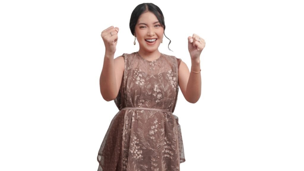 A joyful woman in a brown plus size dress, smiling with her fists raised in excitement, against a white background