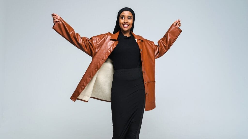 A woman wearing a brown ladies lambskin leather coat with her arms raised, posing confidently
