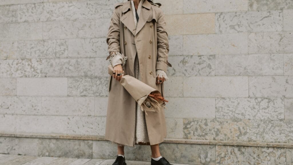 A woman wearing a beige ladies lambskin leather coat while standing near a light stone wall