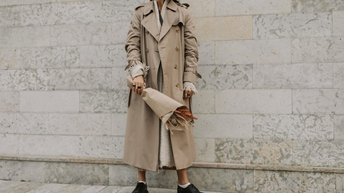 A woman wearing a beige ladies lambskin leather coat while standing near a light stone wall