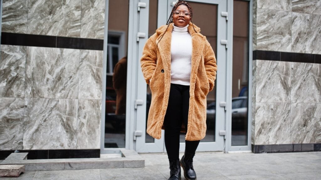Plus-size woman in a stylish brown winter coat standing in front of a modern building