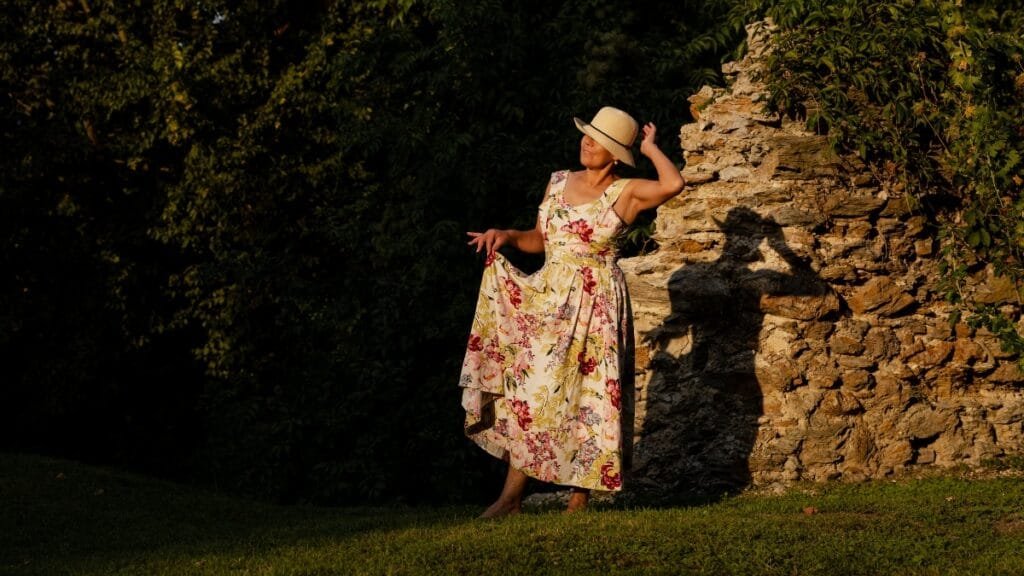 Woman in a floral midi sundress posing near stone ruins during golden hour.