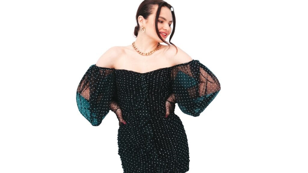 Plus size woman in an off-shoulder black dress with sheer puff sleeves and a stylish chain necklace.
