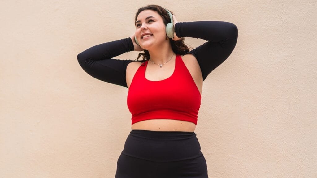 Plus size woman in a red sports bra and black leggings, enjoying her workout with headphones on.