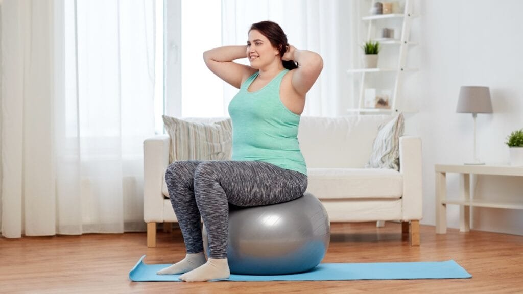 Plus size woman sitting on an exercise ball, wearing sweatpants and a tank top during a workout
