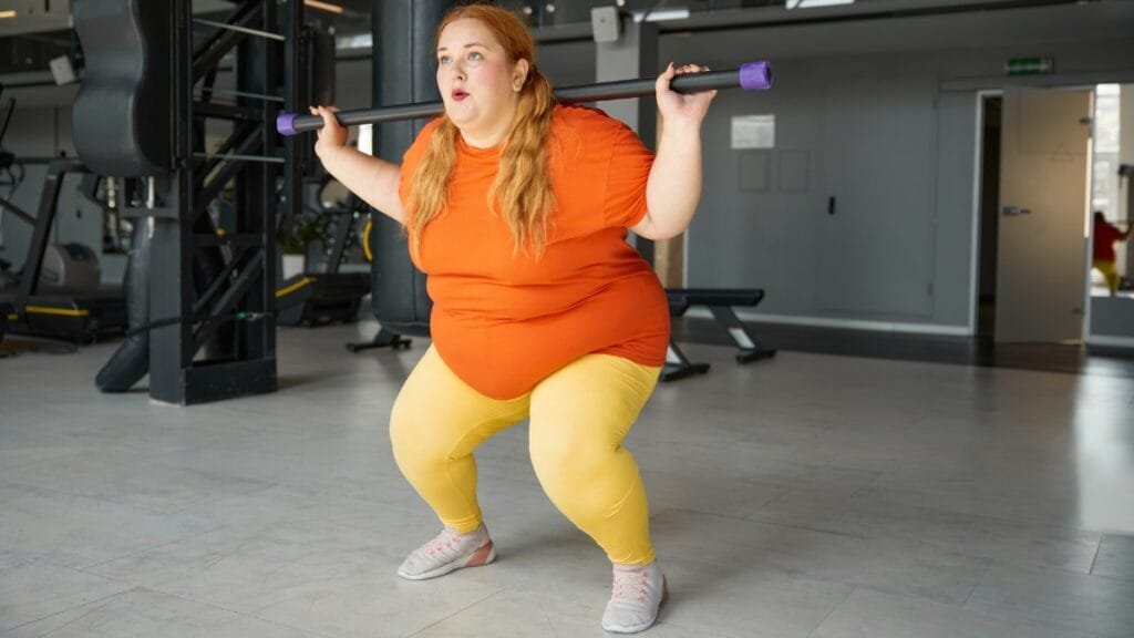 Woman in a plus size workout romper lifting weights in the gym