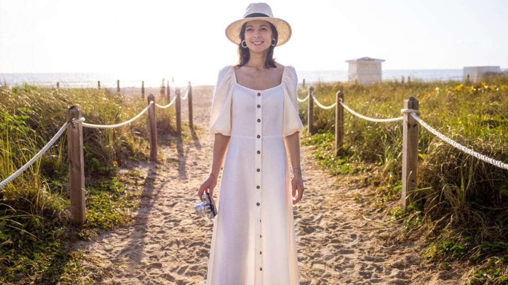 Woman in a white button-down summer midi dress walking along a beach path