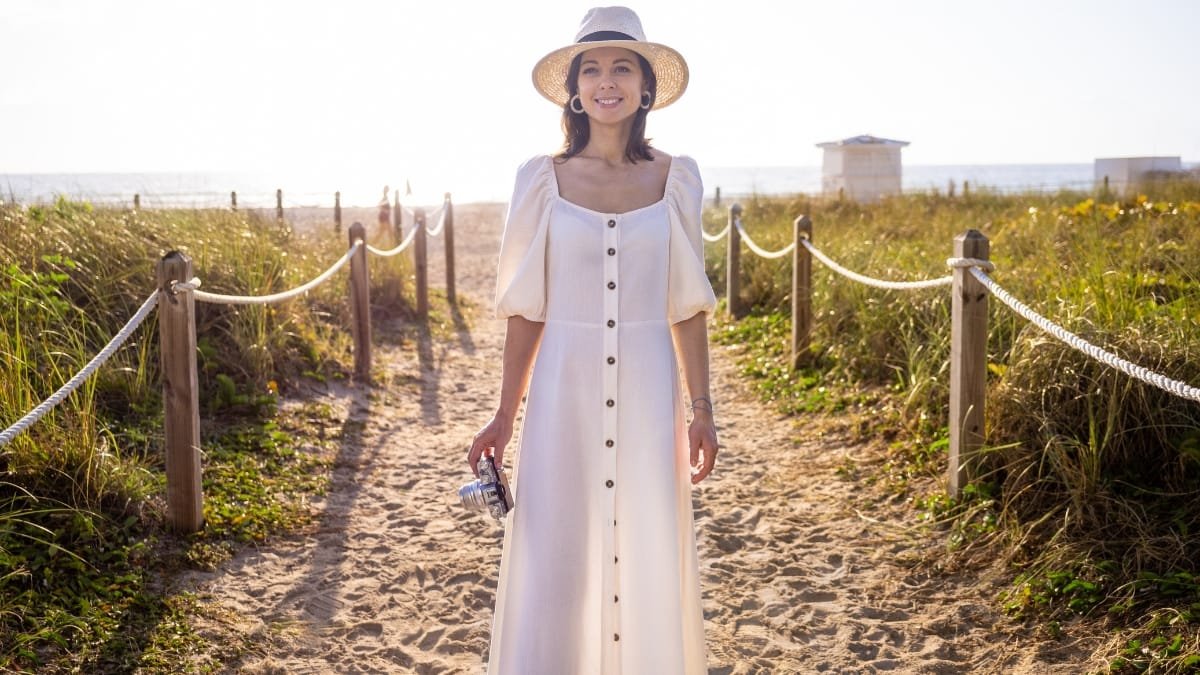 Woman in a white button-down summer midi dress walking along a beach path
