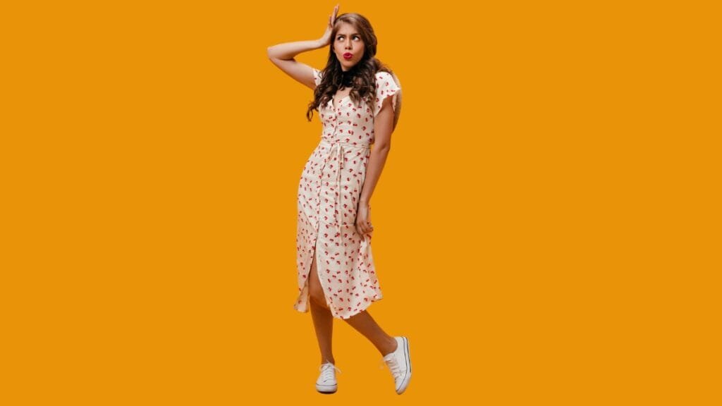 Woman in a floral summer midi dress and sneakers posing in front of an orange background