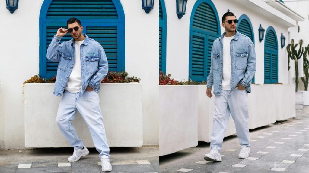 A man wearing a tall denim jacket paired with light denim pants, showcasing a trendy casual look against a vibrant background