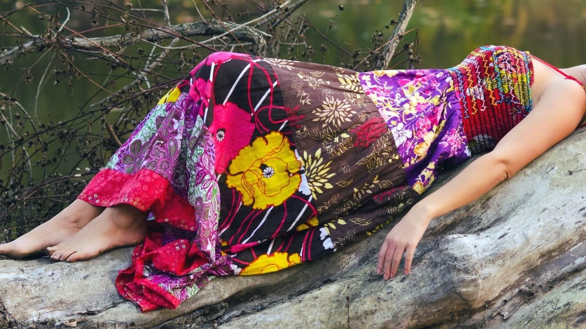 Woman lounging on a log in a colorful velvet floral dress with vibrant patterns.