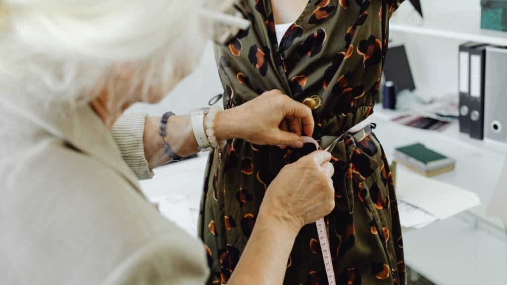 A tailor measures a woman's waist while fitting her dress