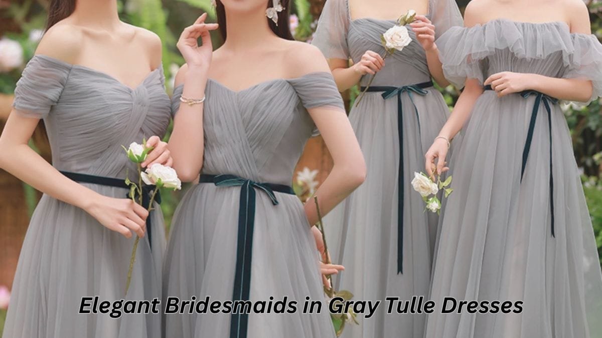 A group of bridesmaids in elegant off-shoulder grey tulle dresses with satin belts, holding white roses.