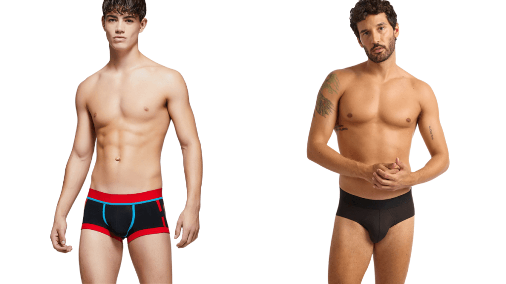 A side-by-side image of two shirtless men wearing athletic briefs. Left: a young man with short dark hair in navy blue briefs with red waistband and red trim. Right: a man with curly hair and a beard in solid black briefs. Both models stand facing forward against a white background.
