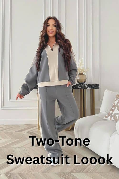 A woman wearing a gray and cream color-block track suit stands indoors, one leg bent, smiling.