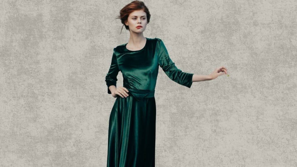 Woman in a green velvet fall dress posing by a white railing in a park