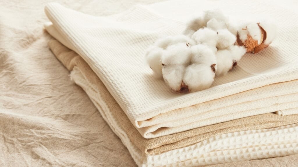Cotton balls placed atop neatly folded cotton fabrics in soft beige and cream tones
