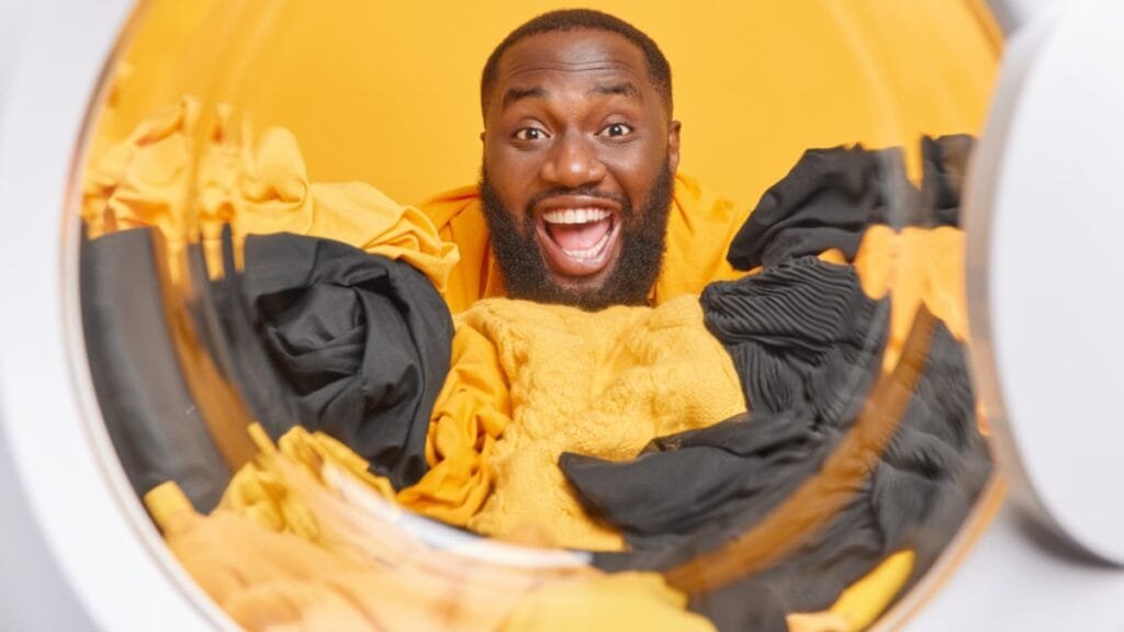 Man excitedly surrounded by clothes in a washing machine, emphasizing wool care