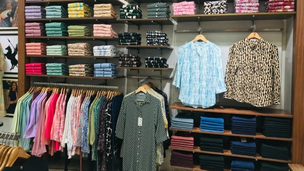 Variety of folded clothing displaying different colors and patterns, showing diverse fabric compositions in a retail store.