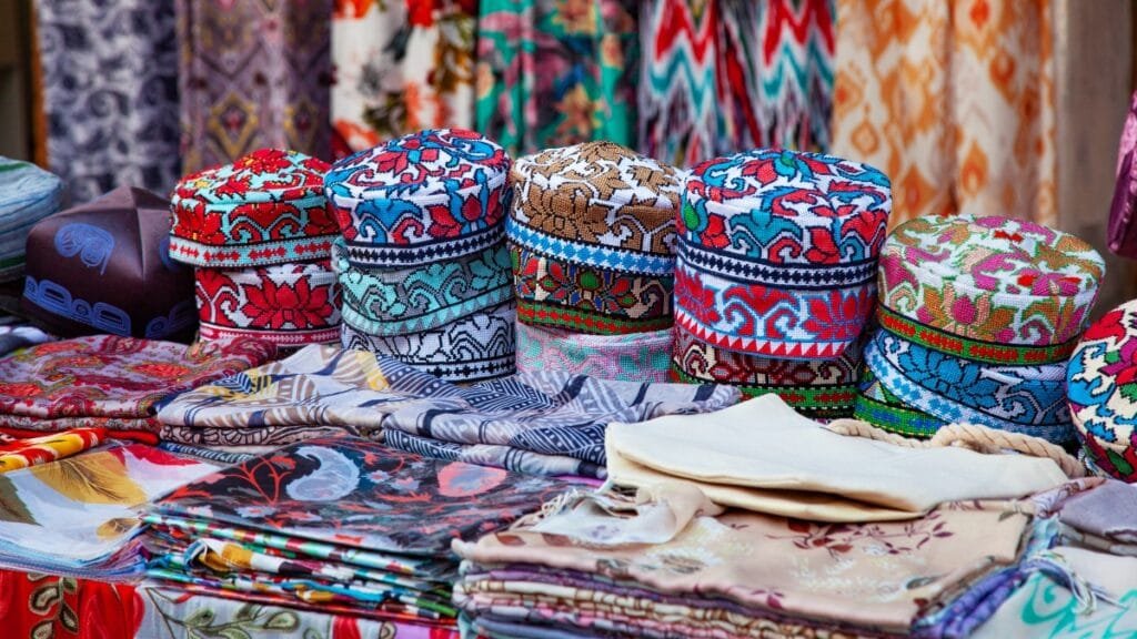 A table display of colorful patterned fabric textile products and decorative hats, representing cultural and sustainable textile choices