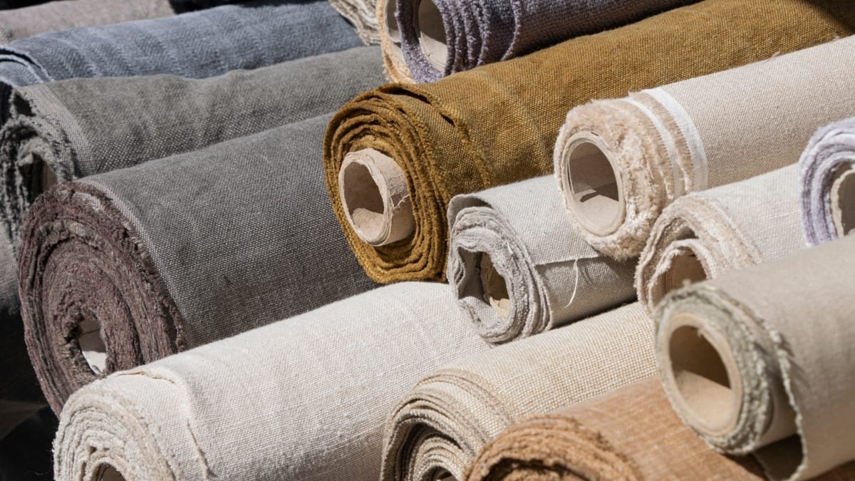 Rolls of upholstery fabric in various colors, showing different textures and materials