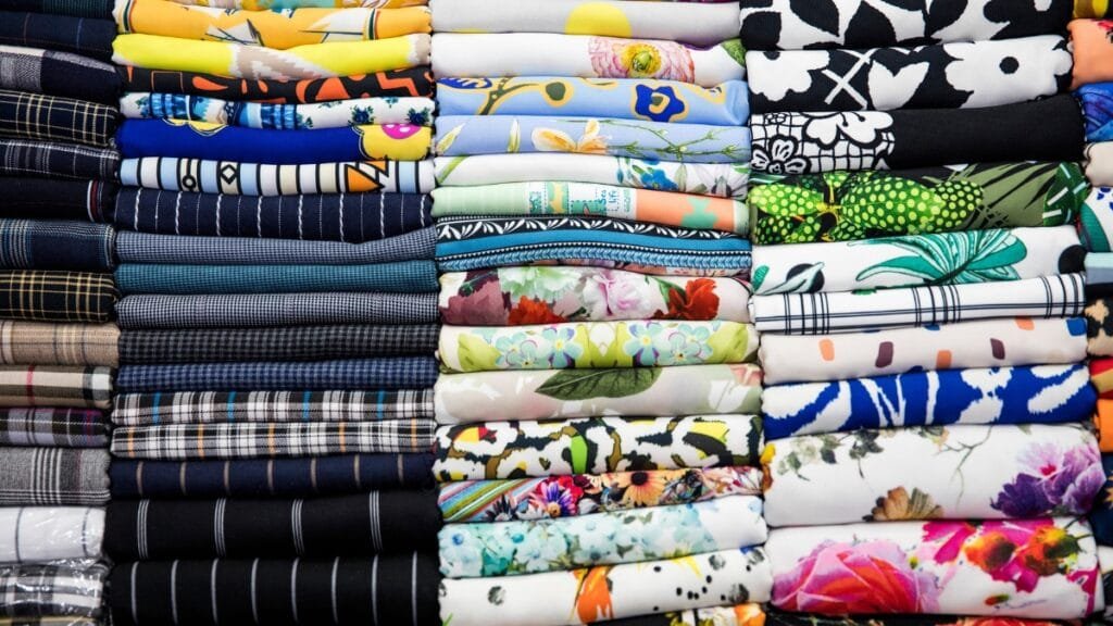 A variety of fabric rolls with floral, plaid, and striped patterns stacked neatly in vibrant colors