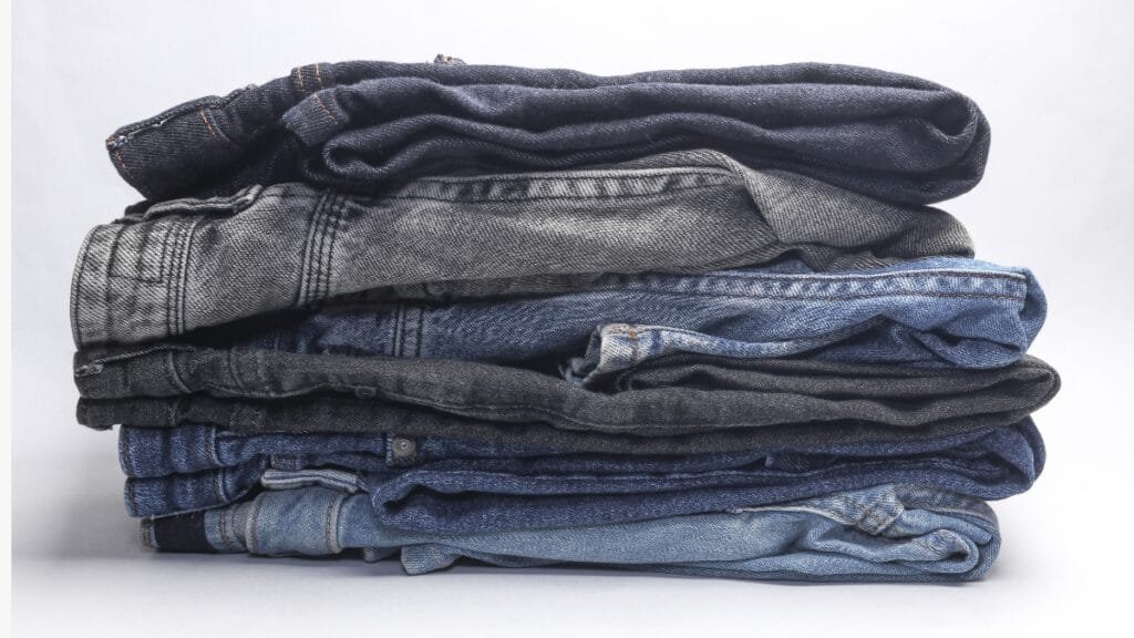 A stack of various denim jeans in different colors and washes, showcasing popular types of pants