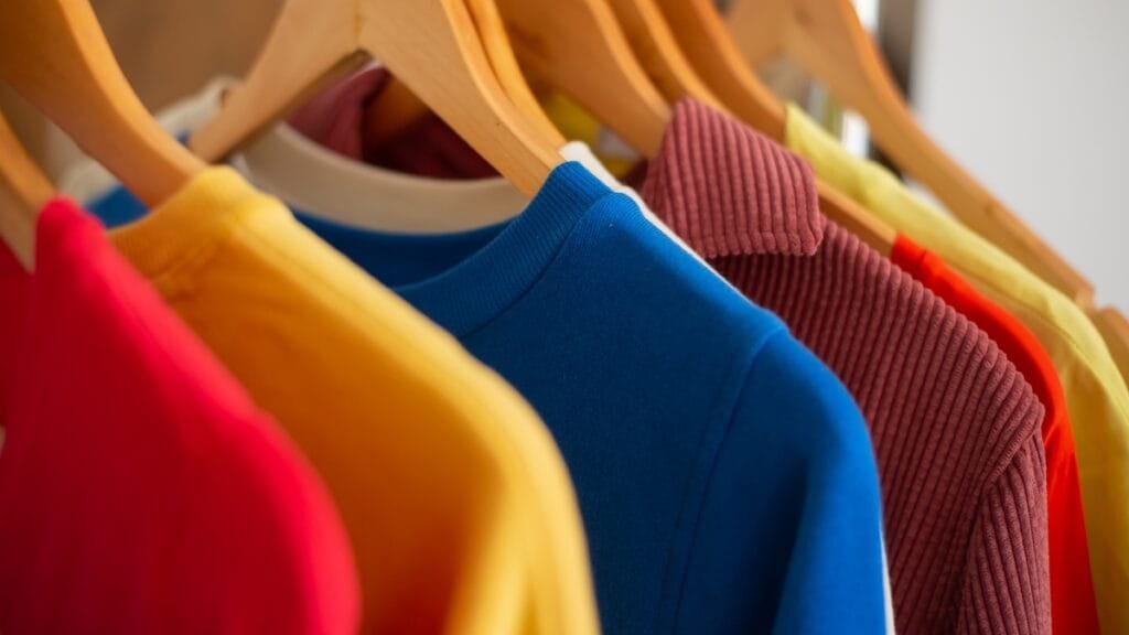 A row of brightly colored shirts hanging on wooden hangers, showcasing the versatility of nylon vs spandex fabric in fashion