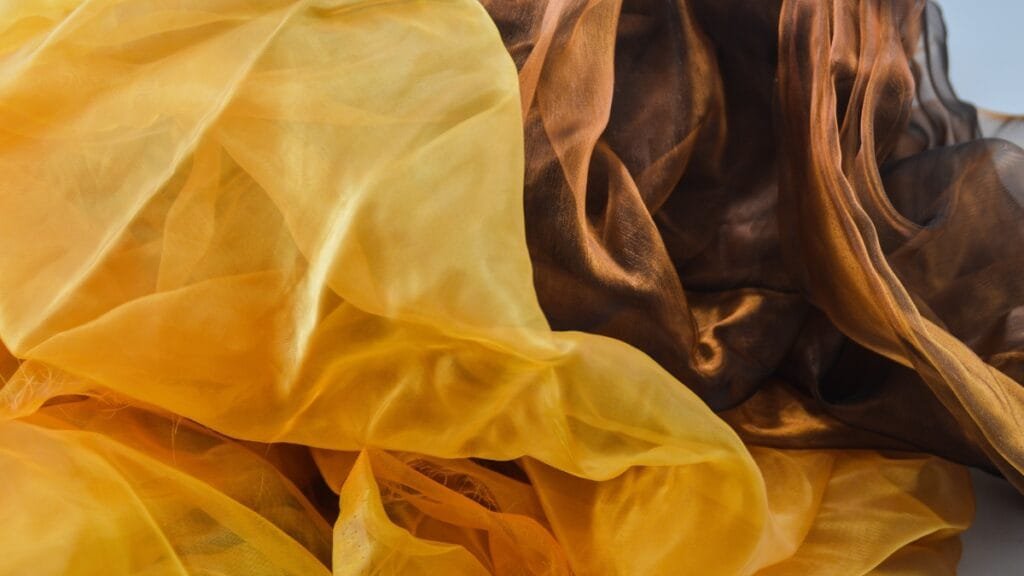 Close-up of sheer fabric in golden and brown tones, showcasing its soft, flowing texture