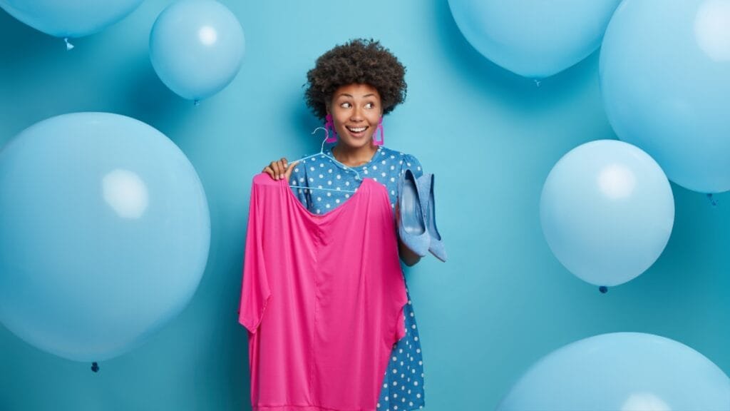 Woman holding a pink stretch fabric dress and blue shoes, representing stylish clothing made with stretch fabric
