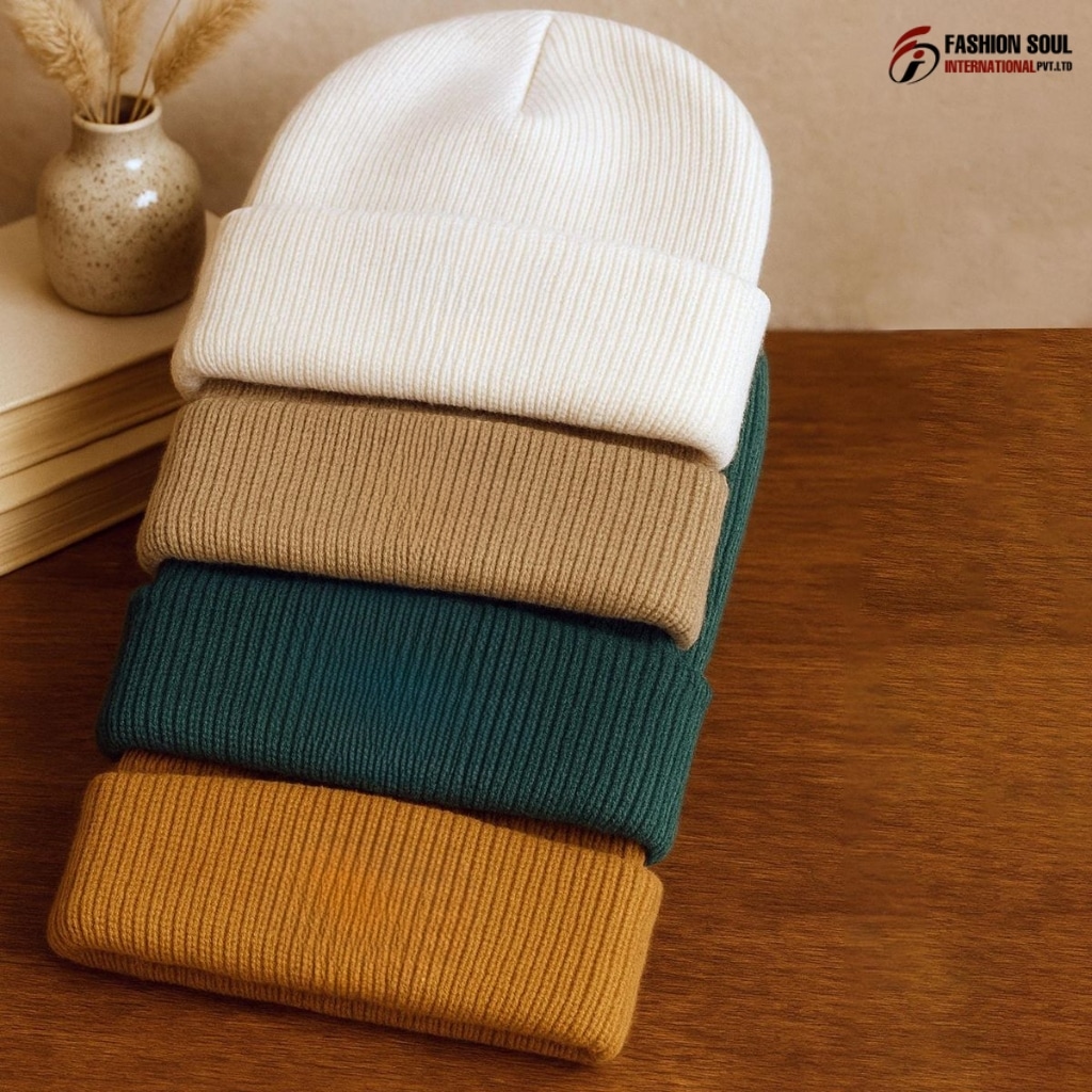 A row of soft, colorfully knitted beanies with varying textures and pom-poms laid out on a wooden table in a sunny Colorado workshop.