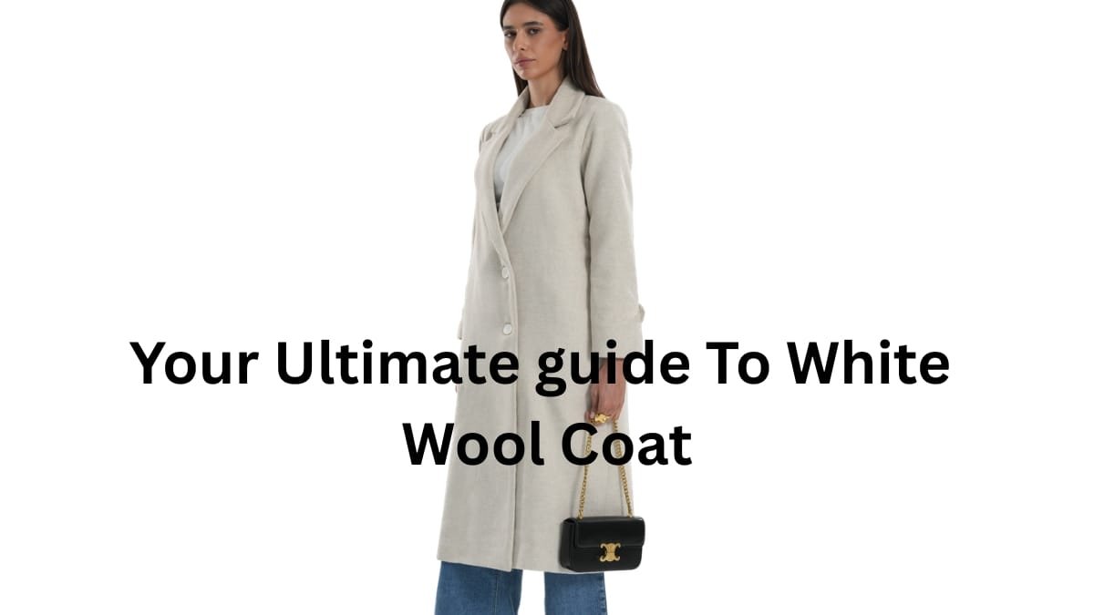 Model wearing a long light-colored wool coat over a white top and blue jeans, holding a small black purse with a gold chain, set against a bright white background.