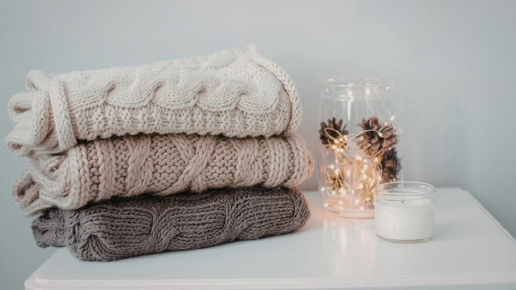 Cozy knit wander mix color shaggy knit hoodie​ stacked with a candle and pinecones for a warm, inviting atmosphere