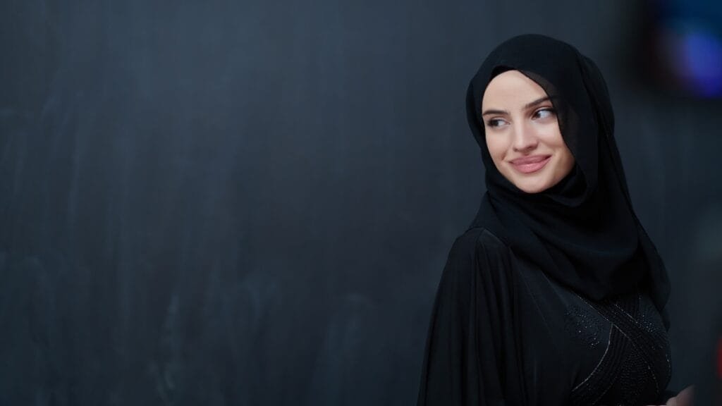 Elegant woman wearing black abaya and hijab set with subtle embellishments against dark background