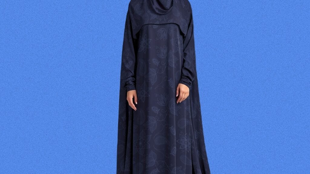 Woman wearing a dark blue abaya against a solid blue background.