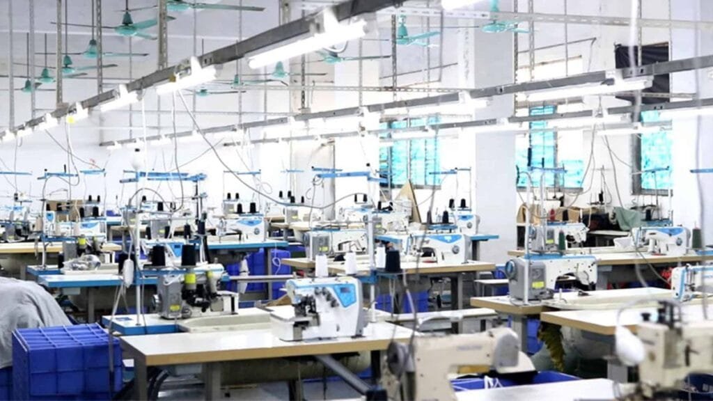 Garment factory interior with rows of industrial sewing machines and workstations used for clothing production.