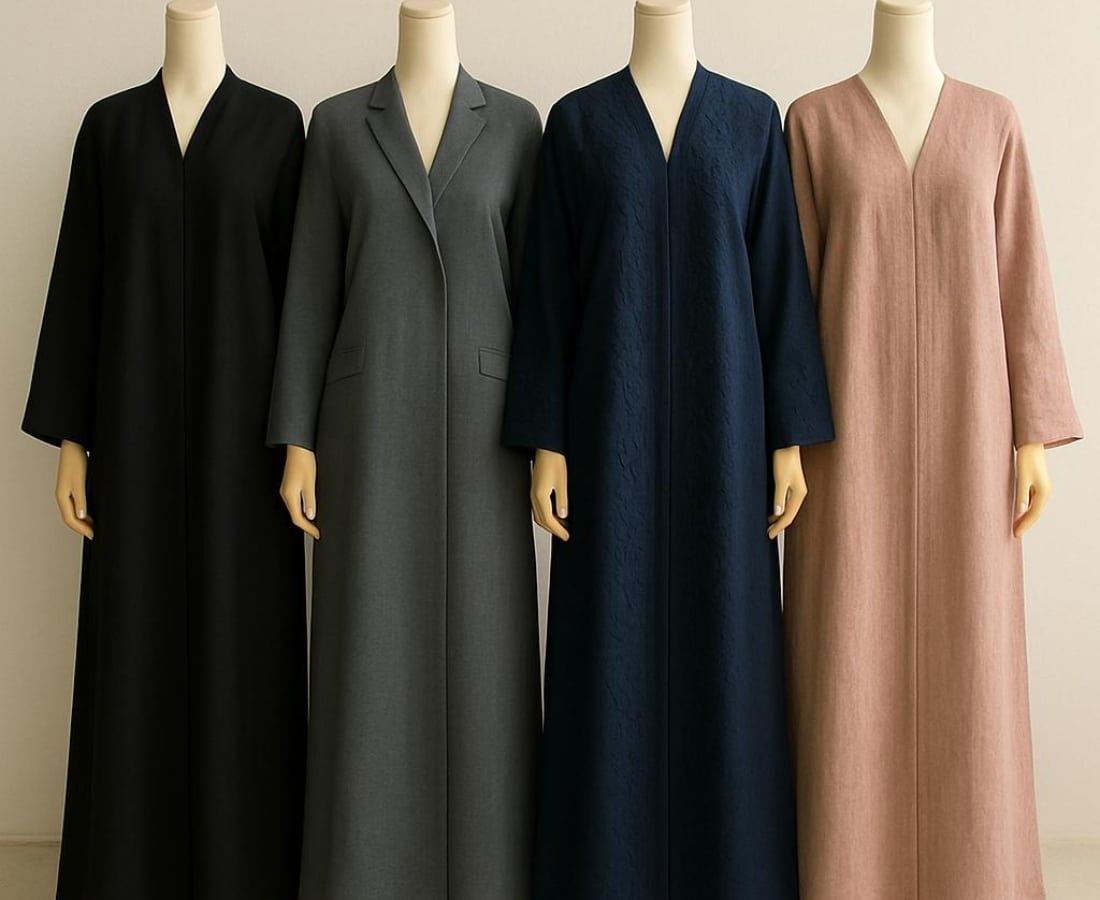 Four mannequins dressed in long, modest abayas in black, gray, navy blue, and dusty pink, displayed against a neutral background.