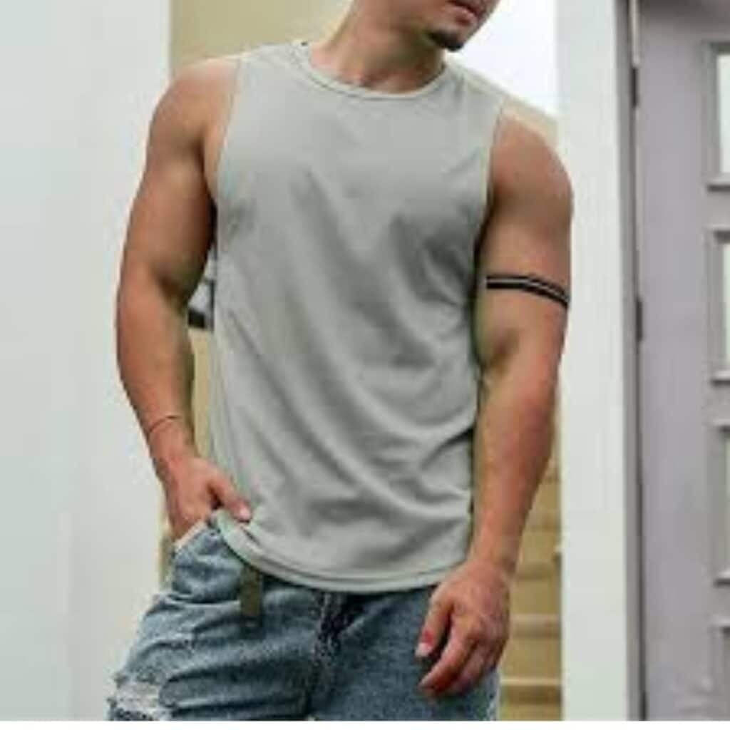 Man in gray tank top and distressed jeans with black armband, standing by a glass-pane doorway.