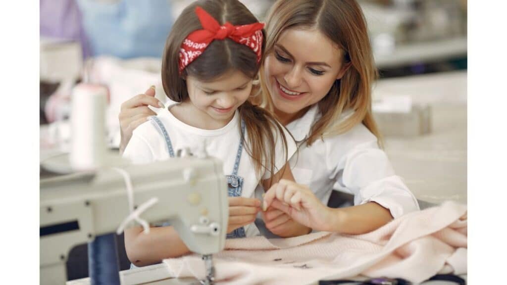 A woman and a young girl sewing pink fabric together at a table with a sewing machine.