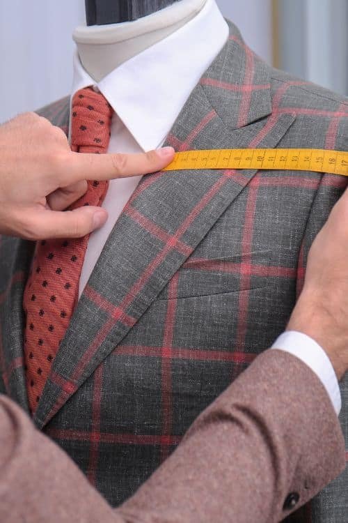 A tailor measuring the shoulder width of a plaid suit on a mannequin, highlighting customization in clothing design.