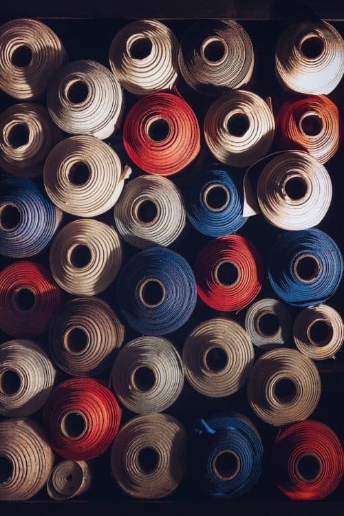 A collection of neatly arranged fabric rolls in shades of white, red, and blue, showcasing textile materials used in garment production.