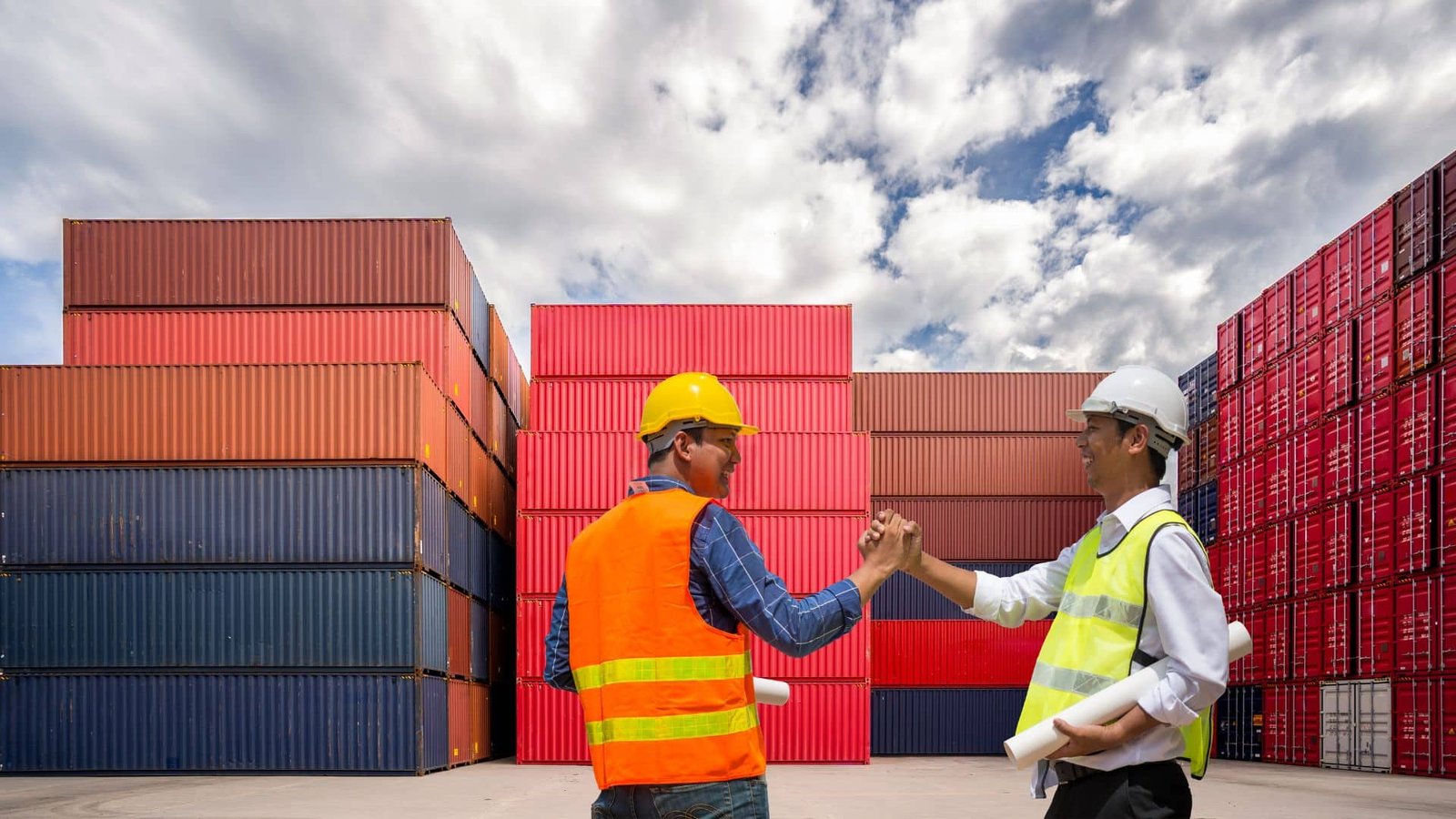 Two workers in safety gear celebrating a successful shipment at a container yard.
